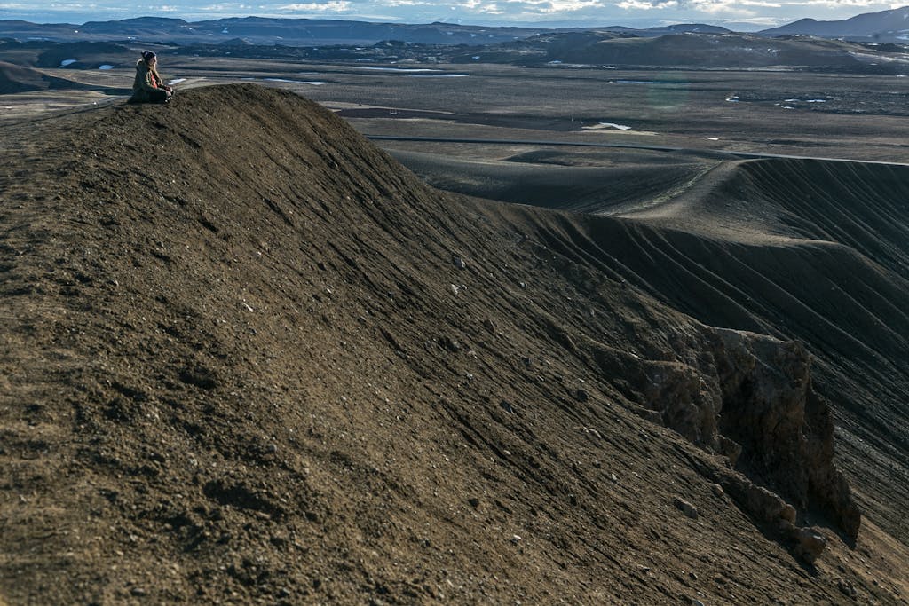 Person sitting and contemplating the vast rugged mountain landscape.